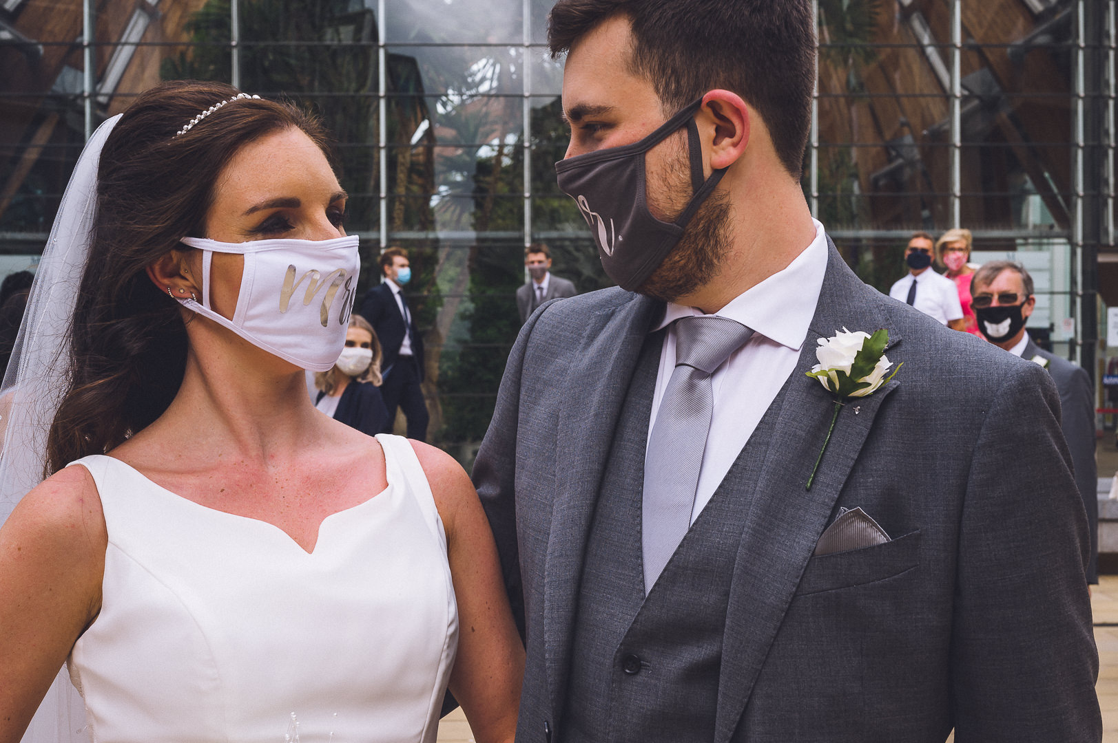 The bride and groom stand together wearing their face masks