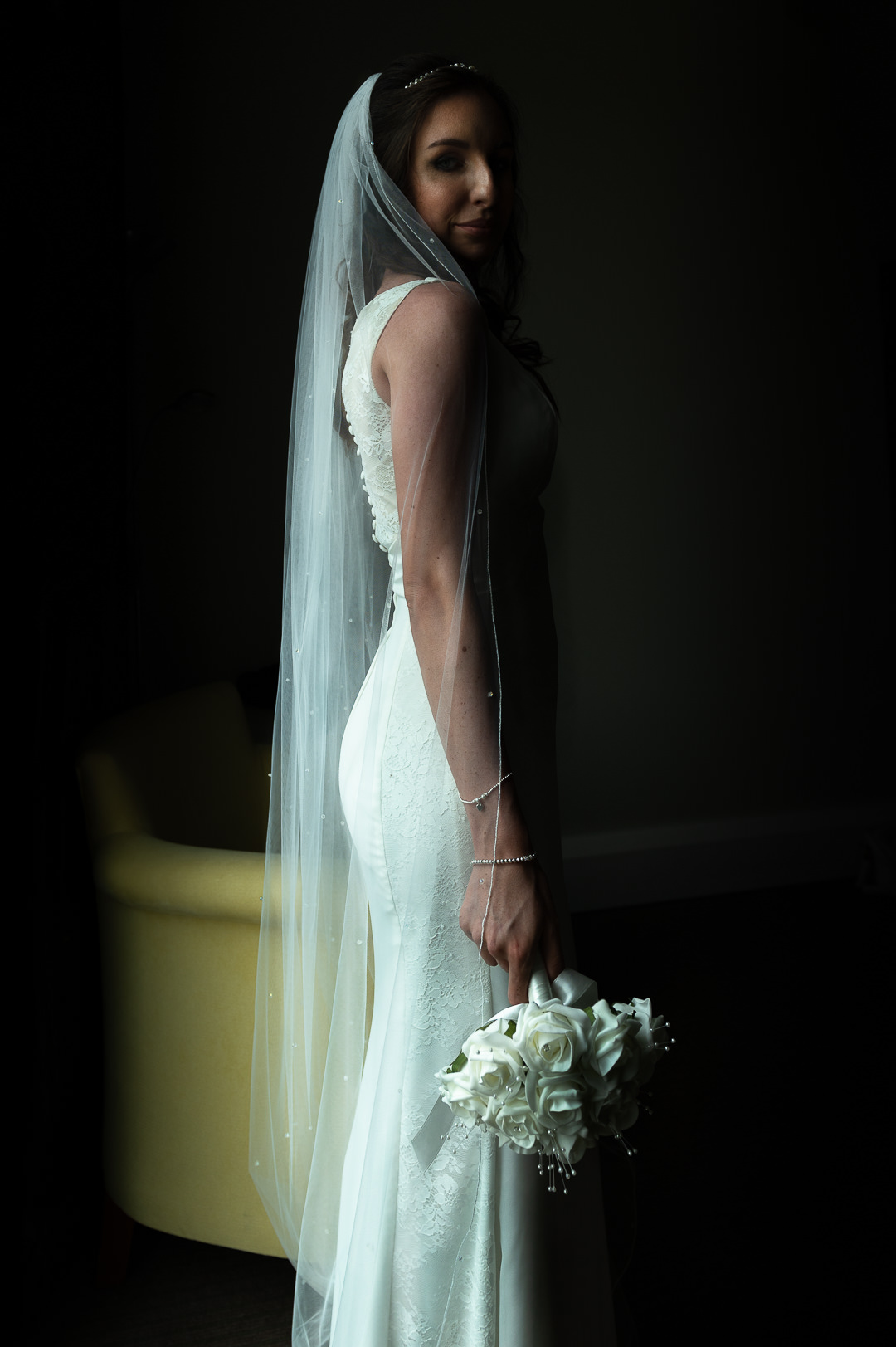 the bride stands with her back to the window light