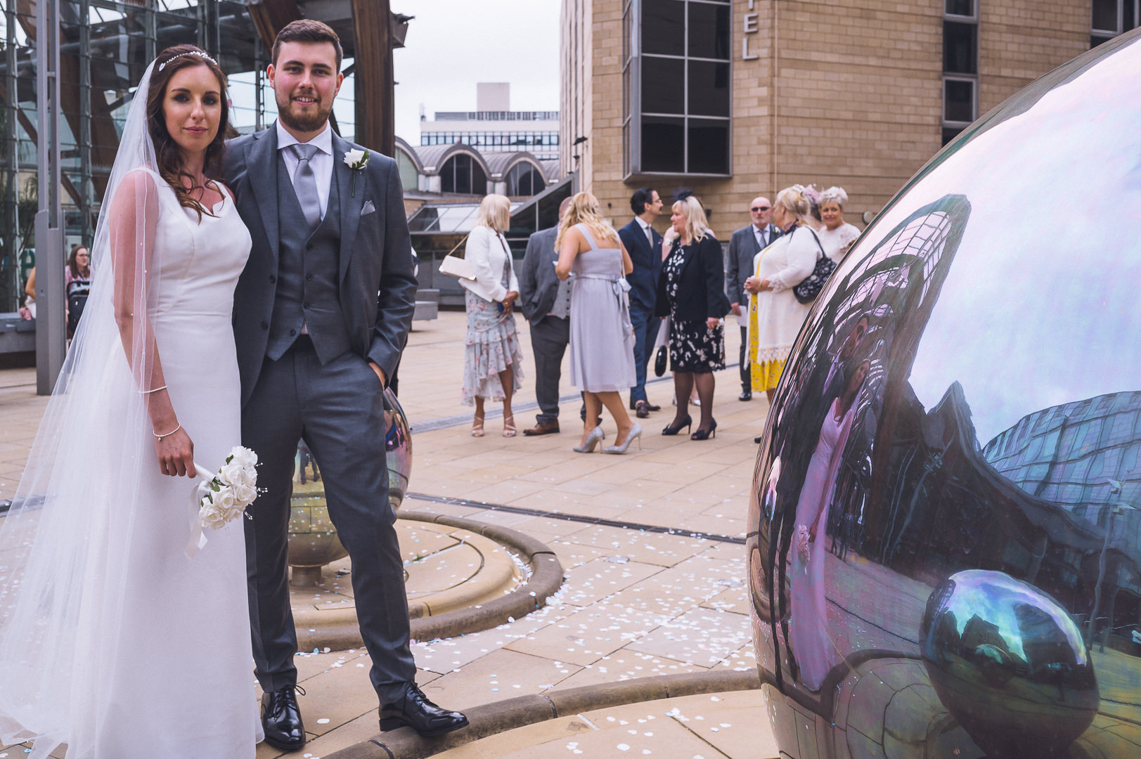 The bride and groom are standing by a large metal ball outside the Winter Gardens