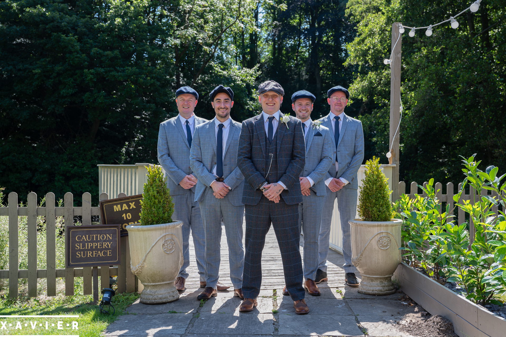 groomsmen stand together wearing suits and flatcaps 