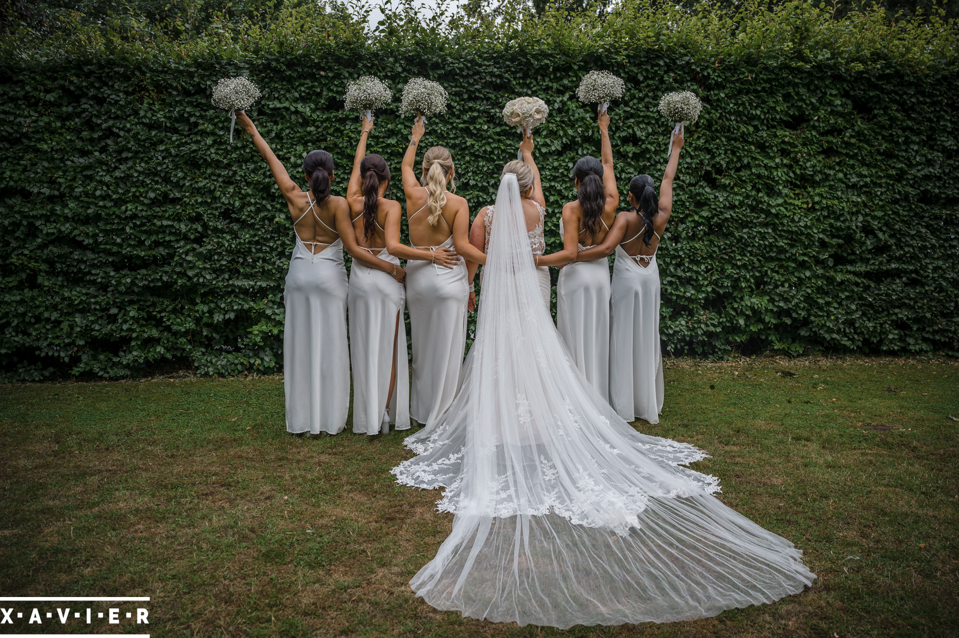 bride and bridesmaids stand in the garden with their backs to the camera