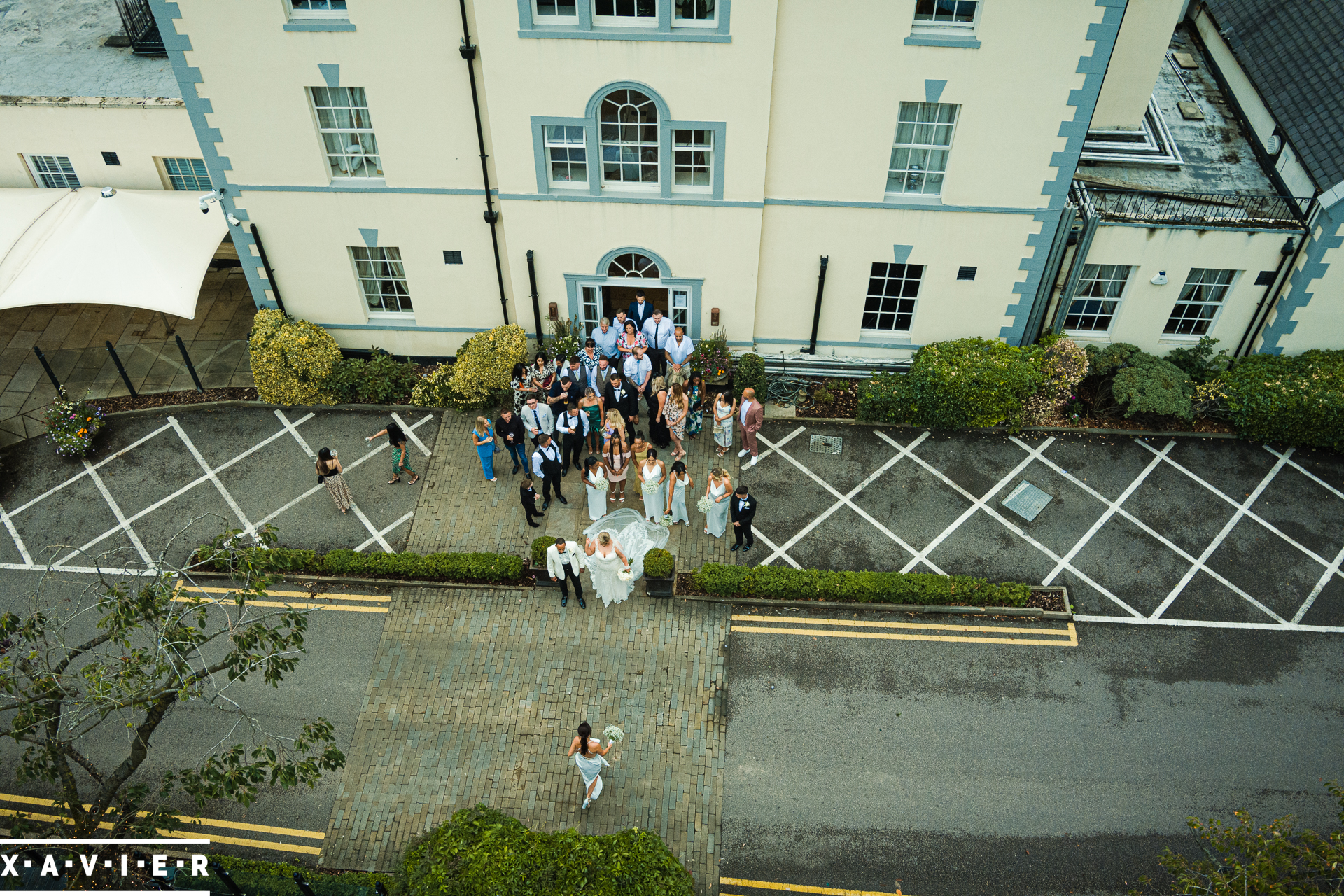 candid drone photo of bride and groom with guests outside the hotel 