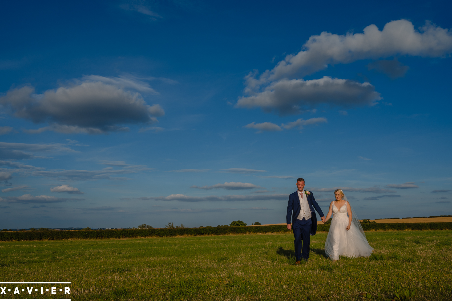 bride and groom walk across fields hand in hand