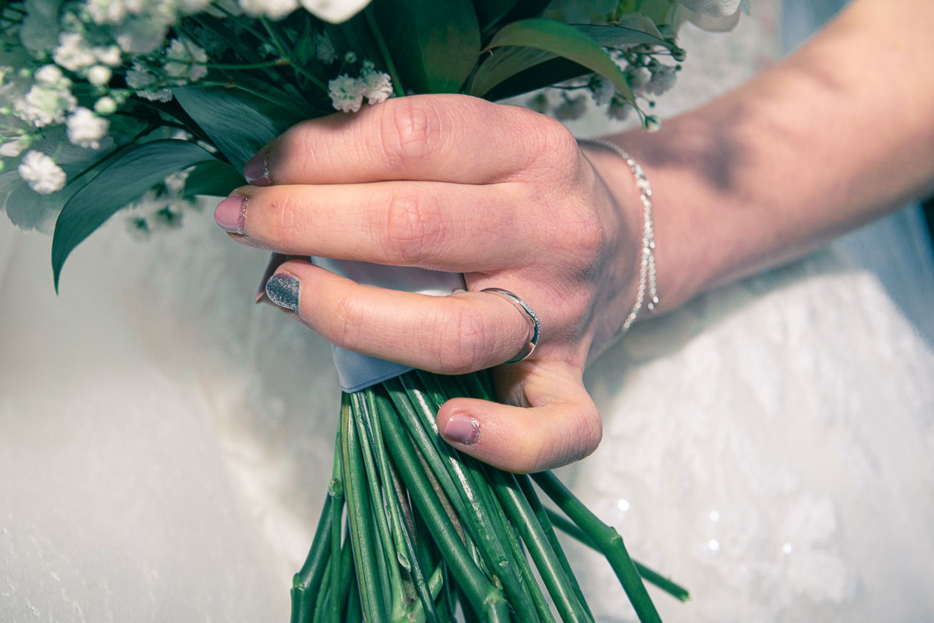 close of wedding ring on brides hand whilst she holds her flowers