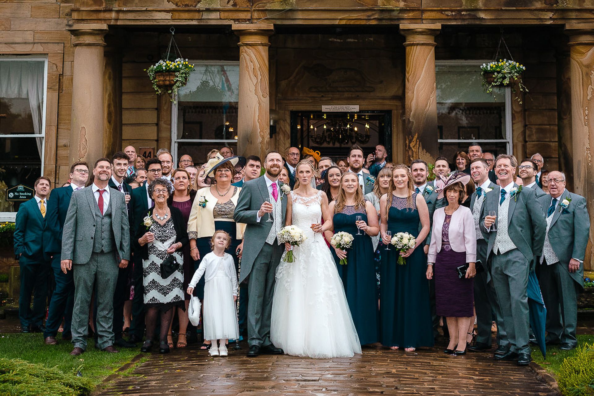 bride and groom stand with wedding party outside walton hall