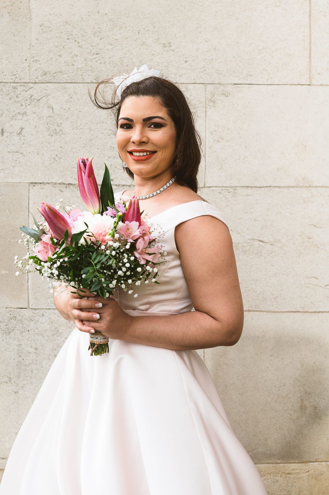 the bride stands with her flowers in front of a stone wall