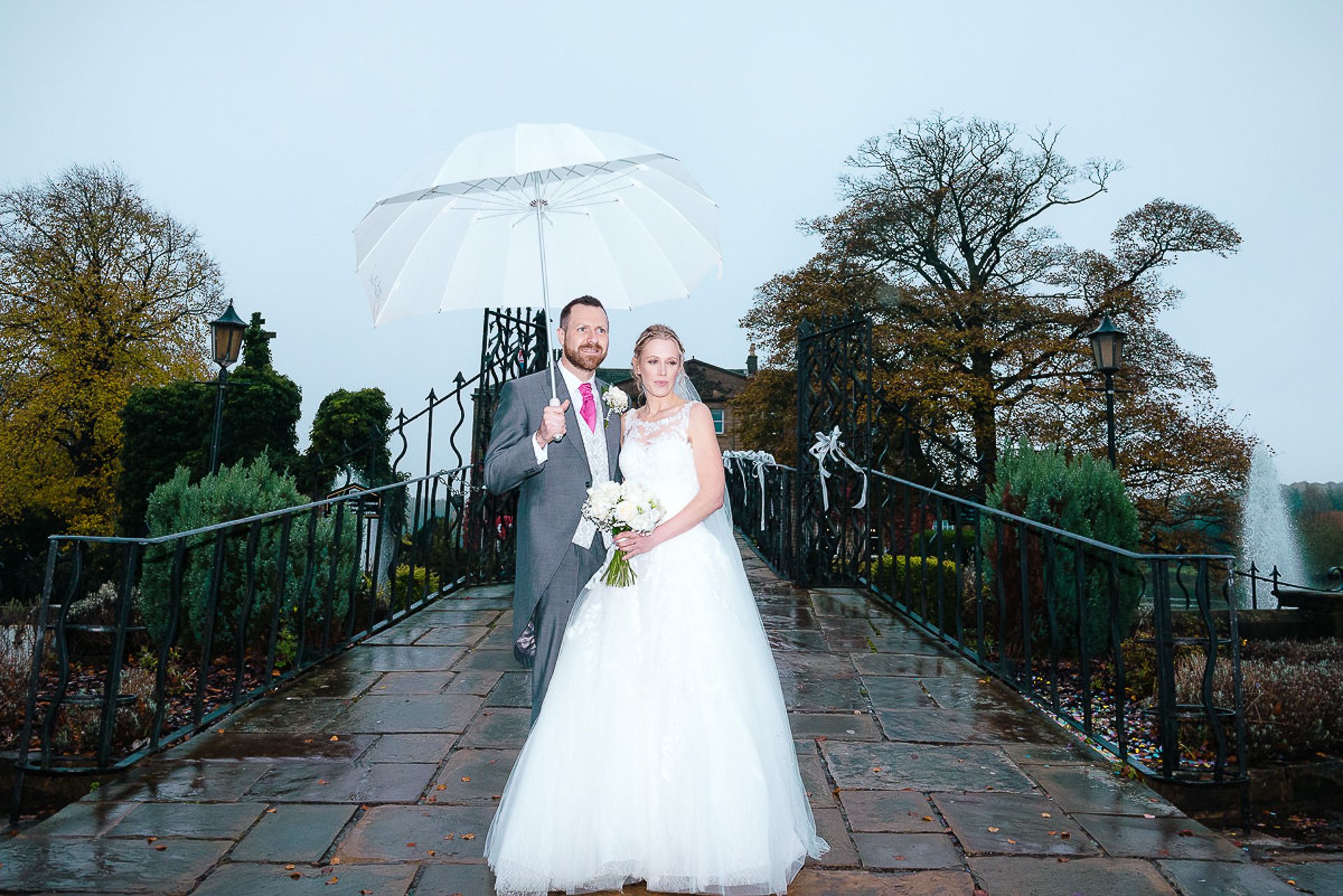 bride and groom stand on the bridge under an umbrella