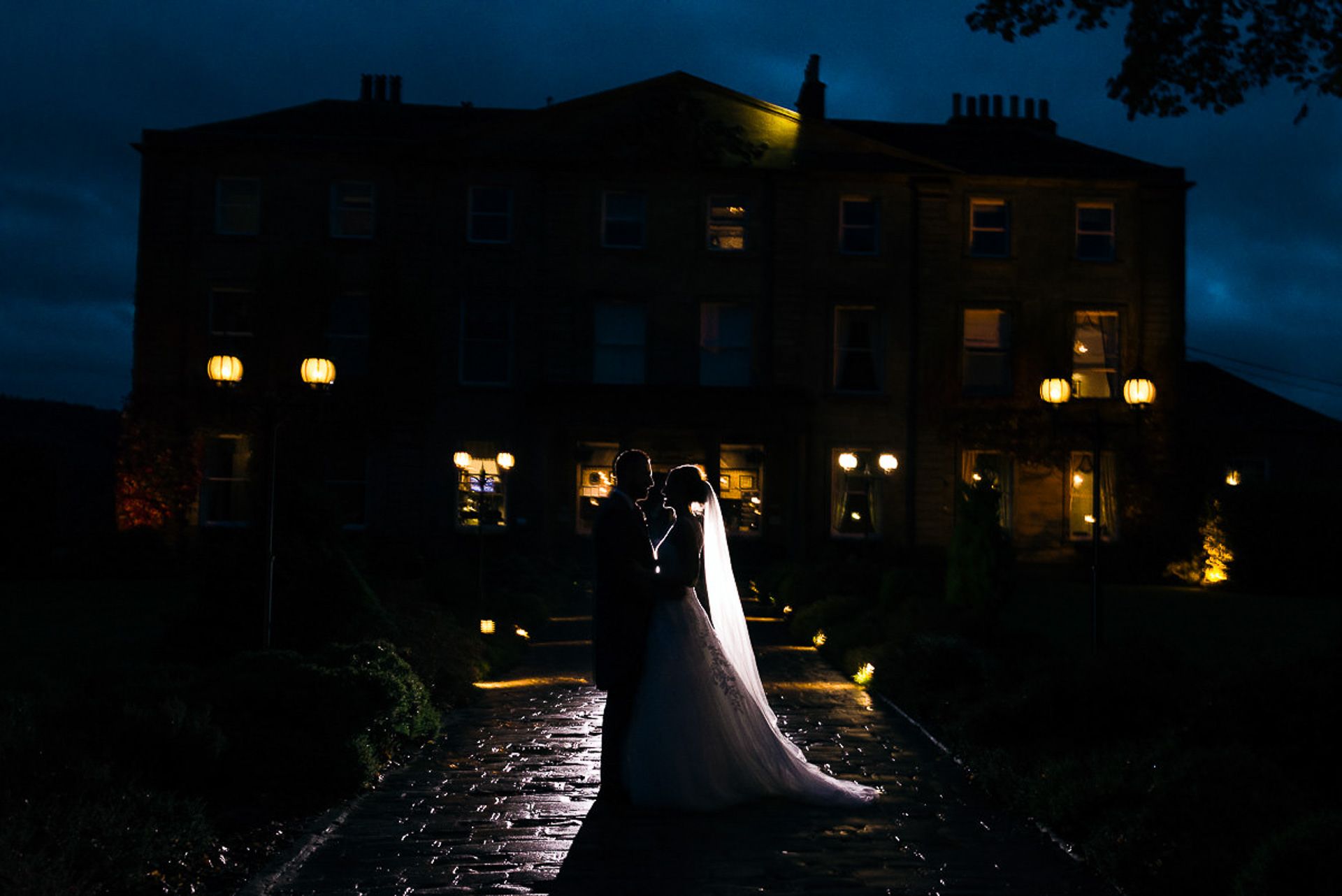 bride and groom stand alone in front of walton hall at night