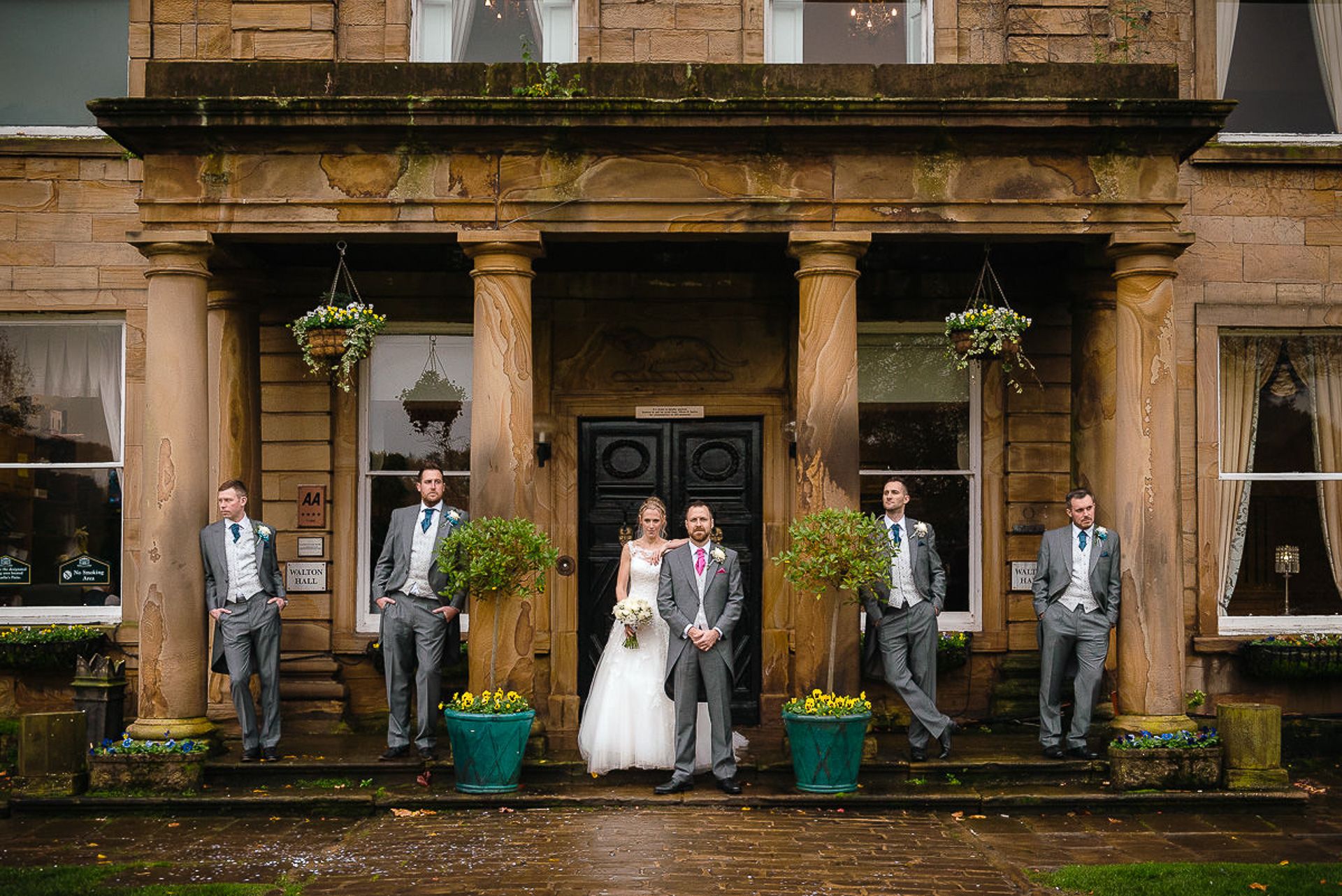 bride stands with groom and groomsmen outside walton hall