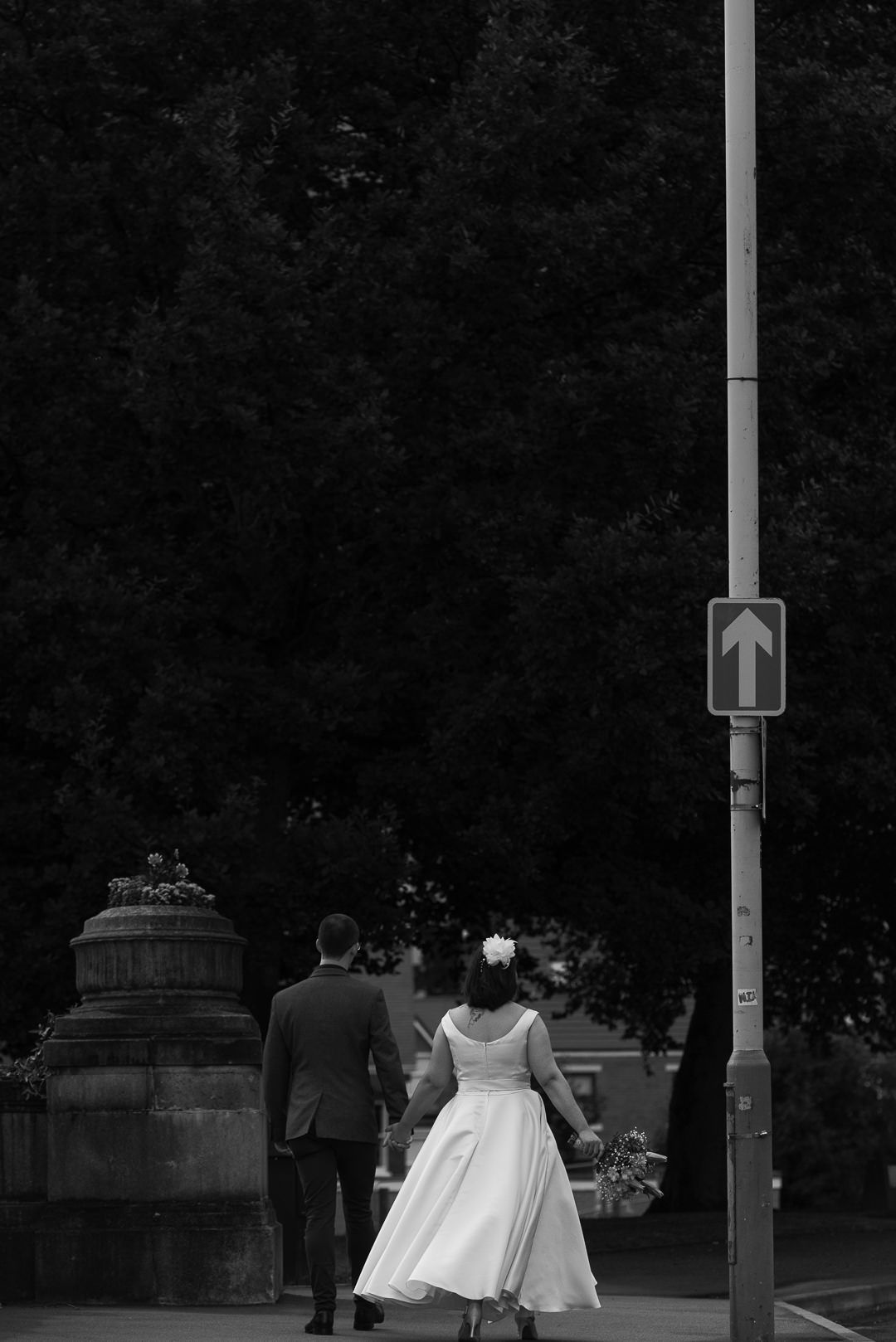 the bride and groom are walking away from the camera down the street with tall trees around them