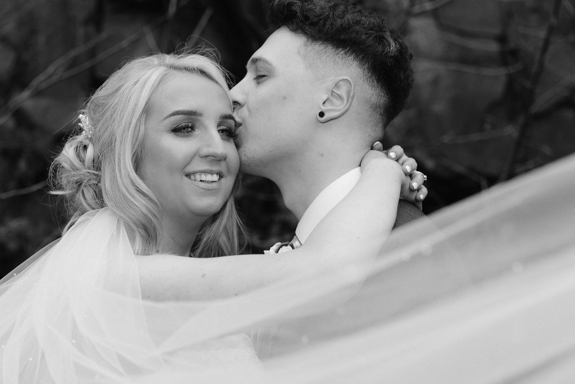 black and white photo of groom kissing the bride on the side of her head