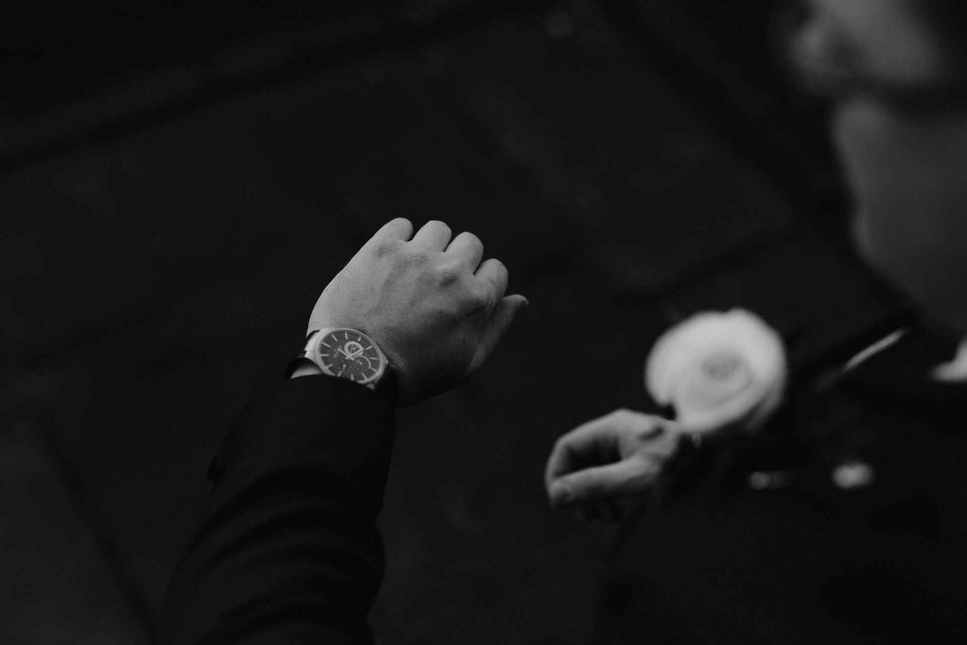 black and white version of an over the shoulder view of the groom looking at his wristwatch 