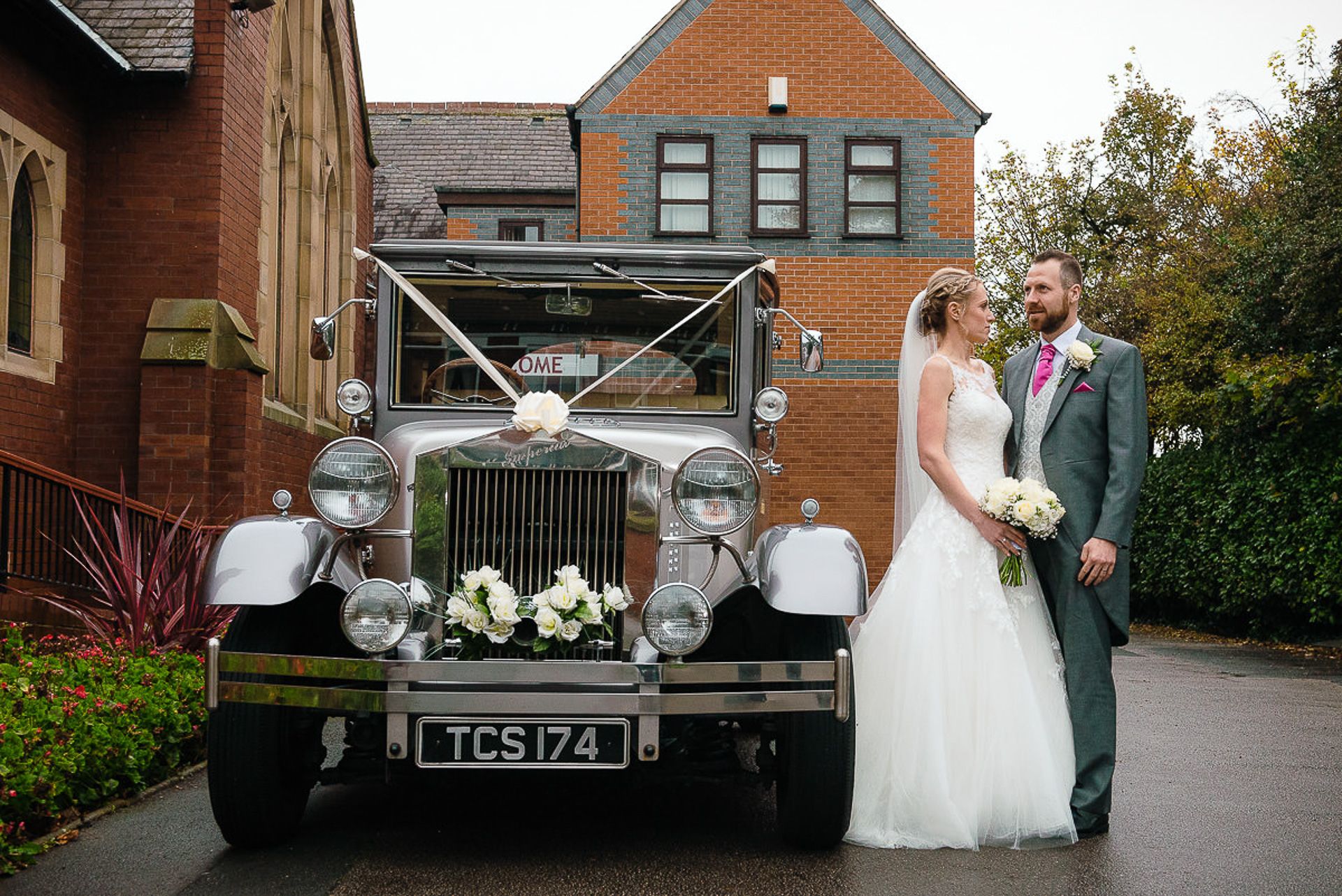 bride and groom stand beside the wedding car ready to leave the church