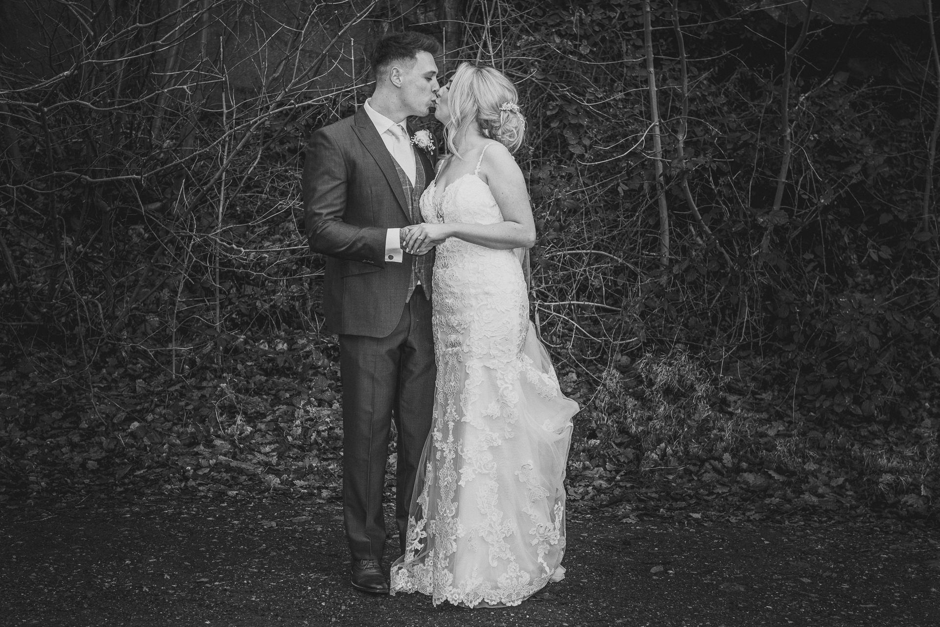 black and white photo of bride and groom kissing in wooded area