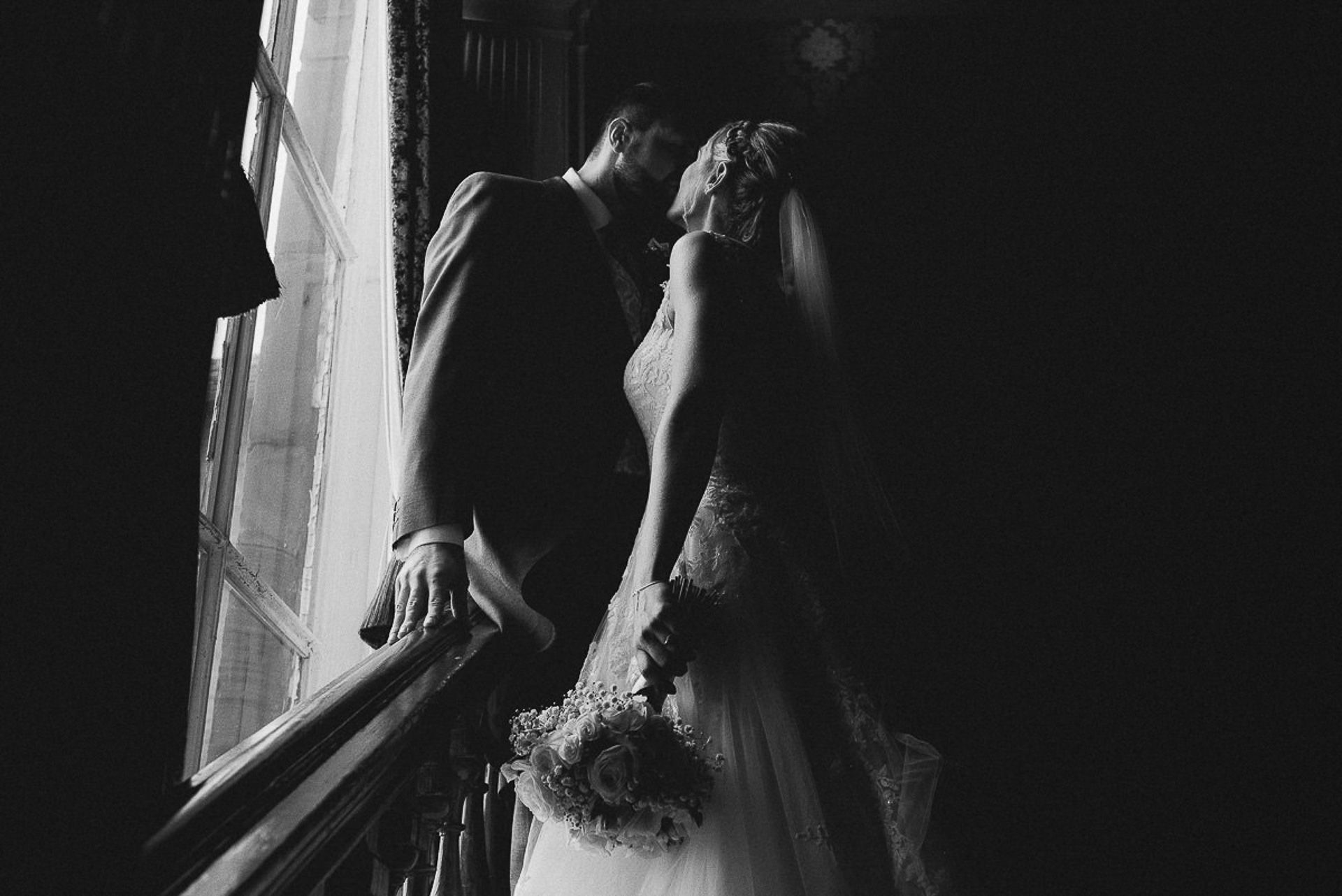 bride and groom are kissing on the stairs in front of the window