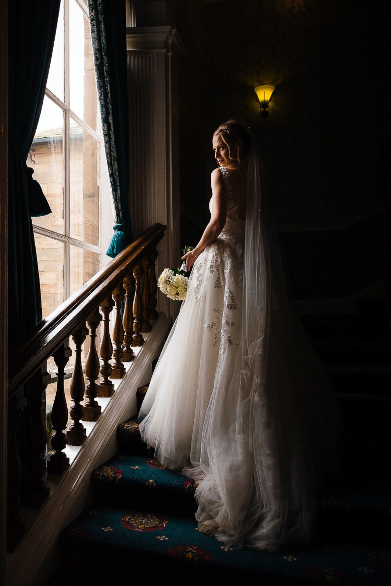 bride stands on the stairs looking out of the window